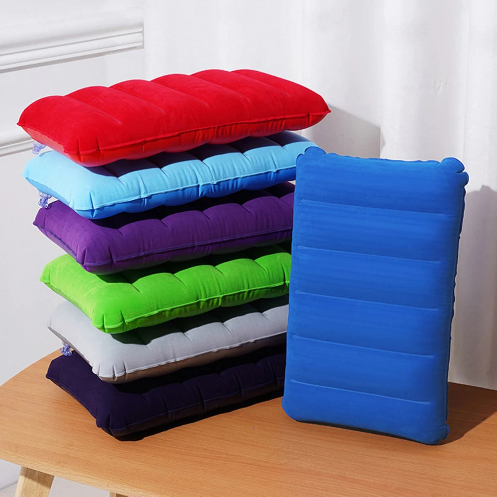 A stack of colorful inflatable travel pillows in various shades of red, blue, purple, and green on a wooden surface.