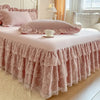 A pink lace ruffled bed skirt set covering a bed with pink pillows and white bedding.