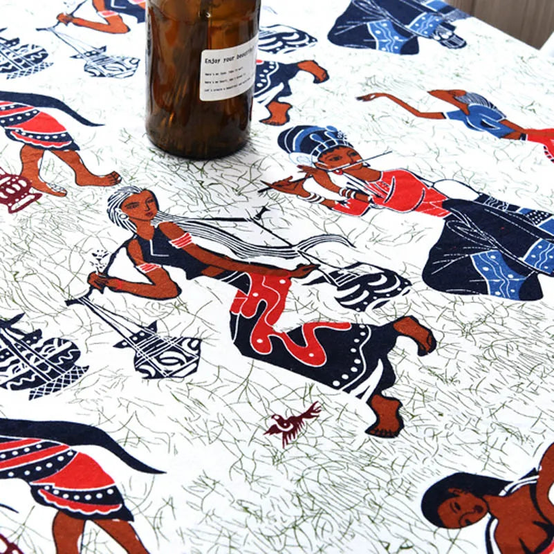 A close-up of bohemian printed linen fabric featuring colorful tribal figures and patterns on a white background.