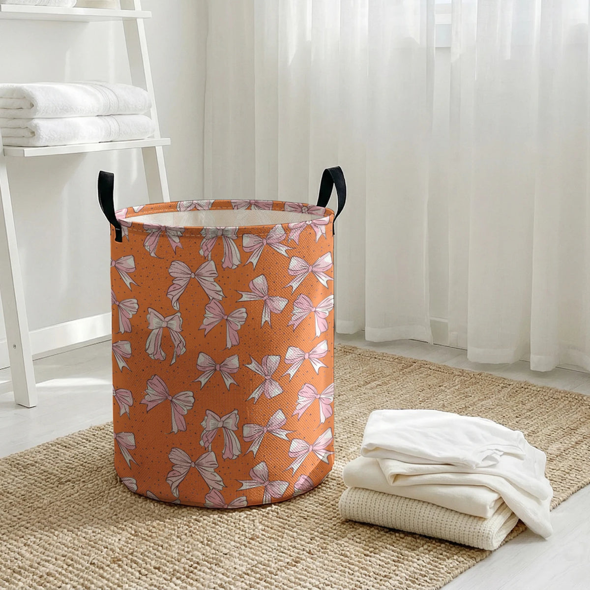An orange canvas laundry basket with a floral bow pattern sits on a woven rug next to white folded towels.