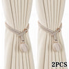 A pair of beige pearl curtain tiebacks with decorative rope ties and gold accents.