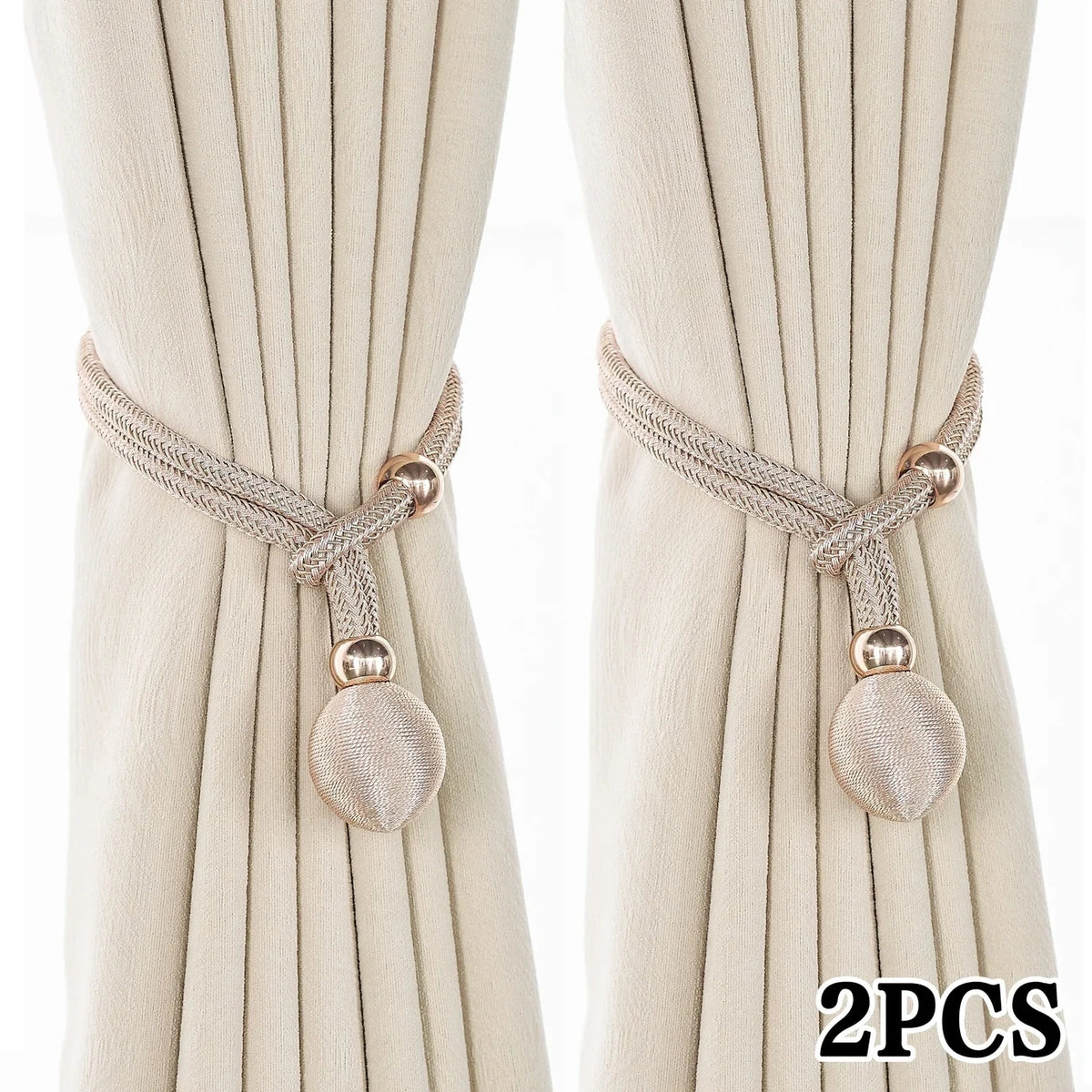 A pair of beige pearl curtain tiebacks with decorative rope ties and gold accents.