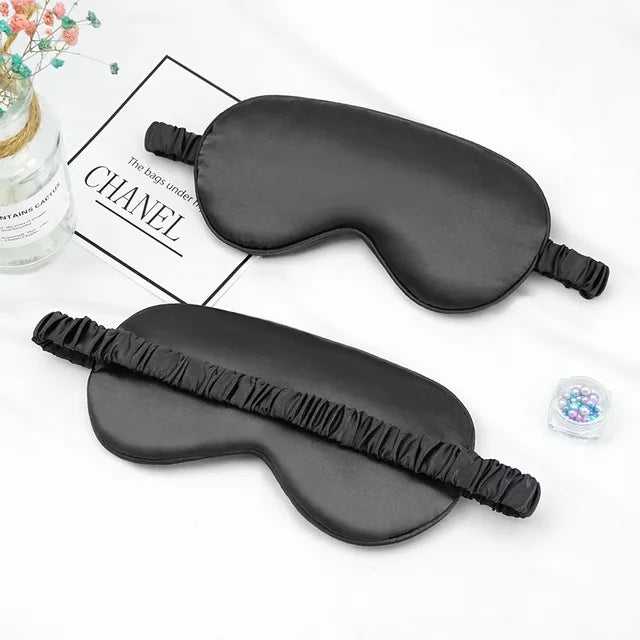 A black silk sleep mask is shown on a white background next to a Chanel branded box.