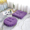 A purple tufted corduroy floor seat cushion resting on a light gray patterned rug near a window.