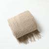 A beige oversized knitted tassel throw blanket with a textured weave.