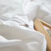 A close-up of a white duvet cover with a silver zipper and pom-pom decoration, folded fabric, and a wooden hanger.