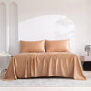 A tan luxury organic bamboo bed sheet set draped on a bed in a bright, minimalist room.