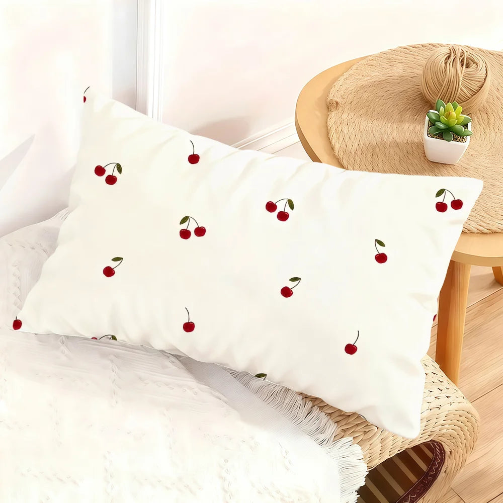 A white cushion cover featuring a pattern of small red cherries on a beige woven surface.
