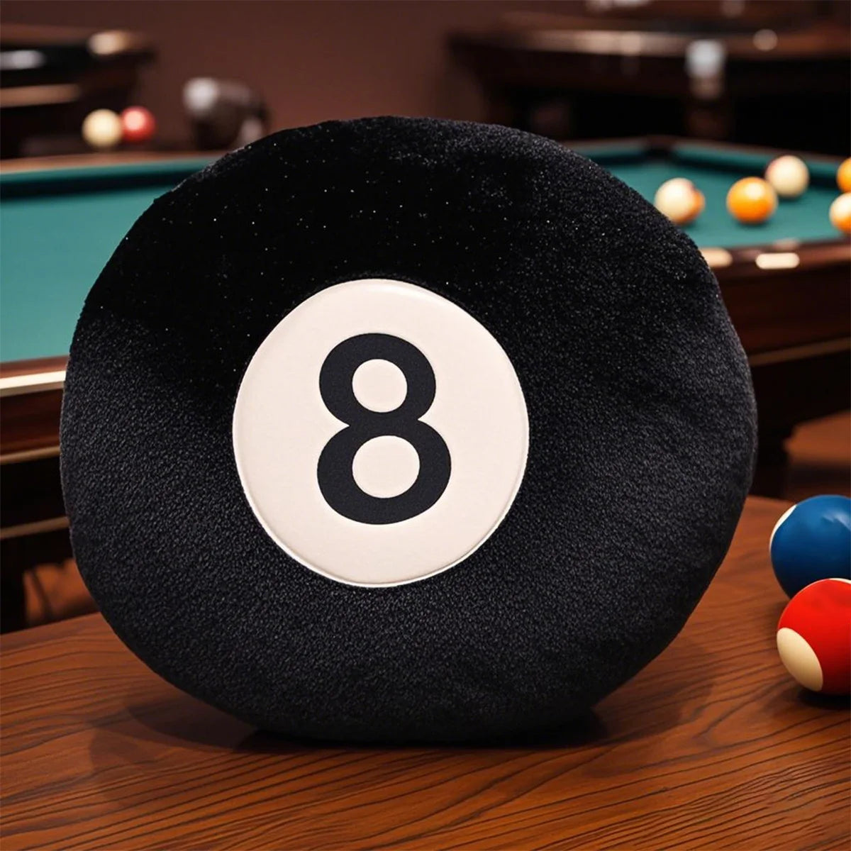A black soft memory foam ball pillow cushion with the number 8 is resting on a wooden table near a pool table.