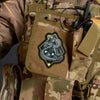 A close-up of a tan camouflage garment featuring a black and yellow snake morale patch sewn onto the fabric.