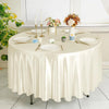 A round table set for an elegant decor featuring a satin cloth, white plates, silverware, and floral arrangements.