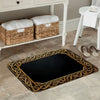 A rectangular dark entrance door mat with a gold woven border rests on a light-colored floor.