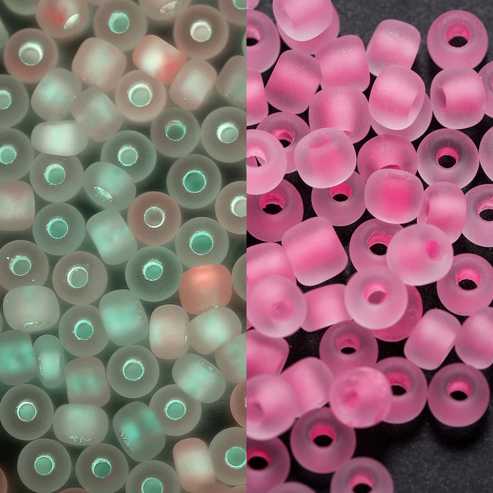 A close-up view of a 600-pack of 3mm glow-in-the-dark glass seed beads in various shades of pink and green.