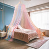 A bed draped with a sheer rainbow mesh mosquito netting canopy in soft pink and blue tones.