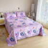 Pink flat bed sheets with a purple floral print displayed on a bed in a bright room.