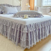 A bed dressed with a lavender lace ruffled bed skirt and white linens.