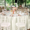 A round table set for an event with white chairs, pink floral arrangements, and elegant place settings.
