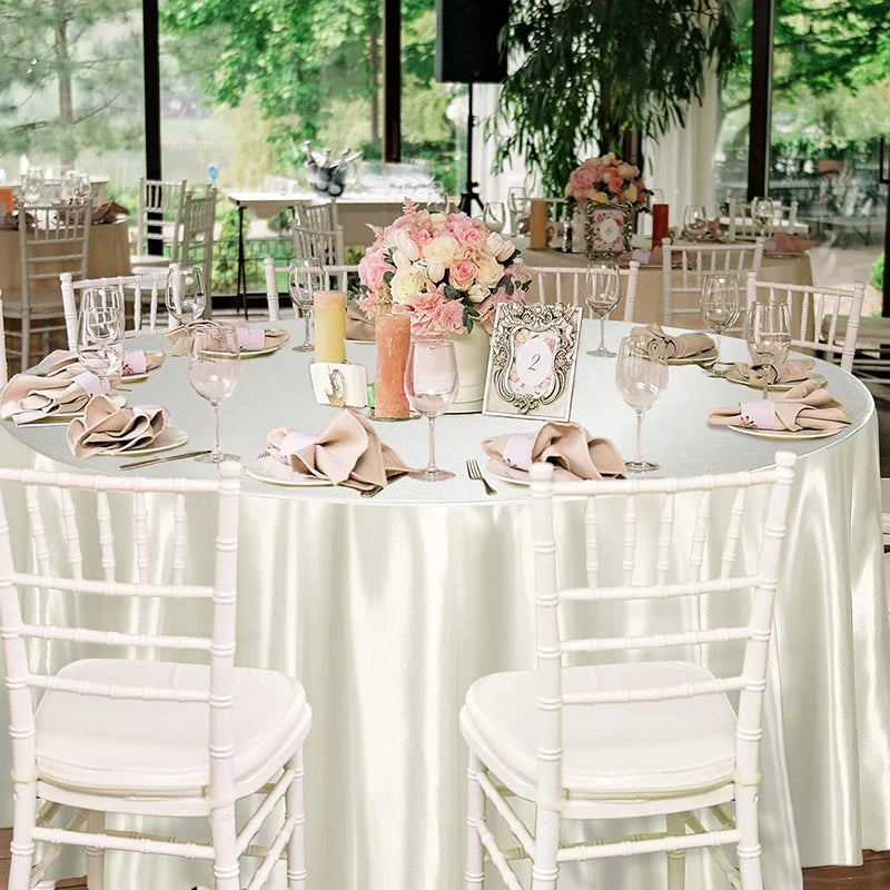 A round table set for an event with white chairs, pink floral arrangements, and elegant place settings.