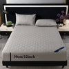 A gray quilted mattress protector is displayed on a bed with dark bedding and pillows.