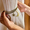 Hands holding a vintage star and moon metal curtain clip attached to a woven cord