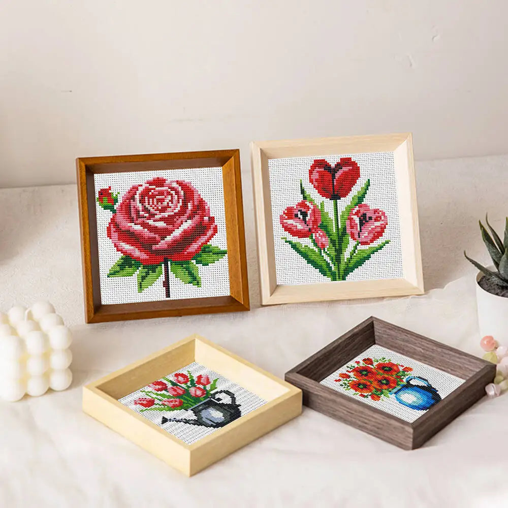 A set of three framed cross stitch floral designs featuring roses and tulips on a white background.