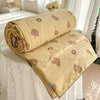 A tan quilt blanket with a pastoral print featuring small brown teddy bears and yellow accents, rolled up on a white bed.