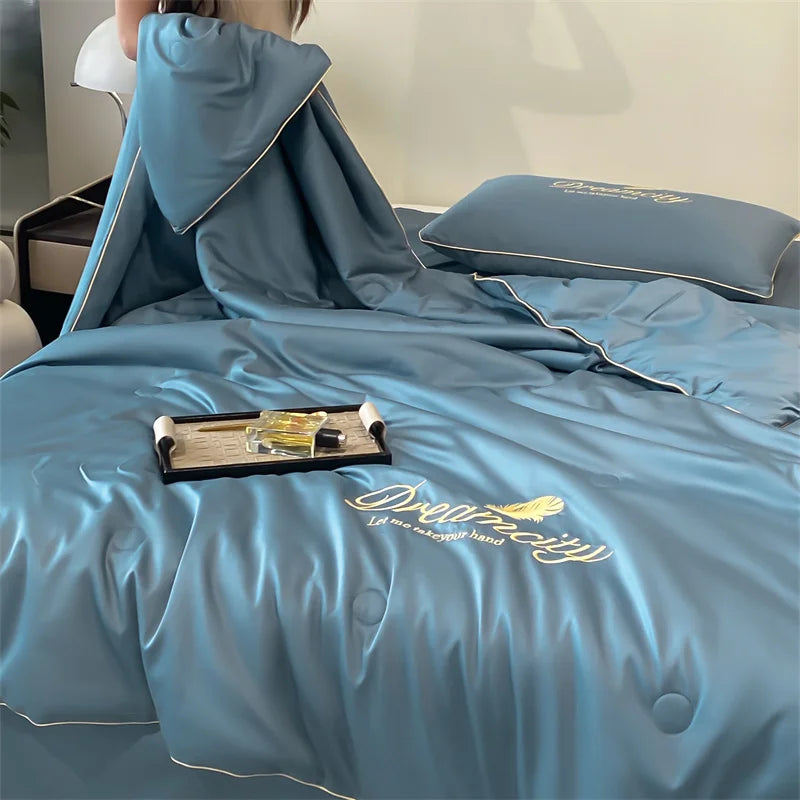 A teal ultra-soft ice silk fiber summer quilt draped over a bed, featuring embroidered text.