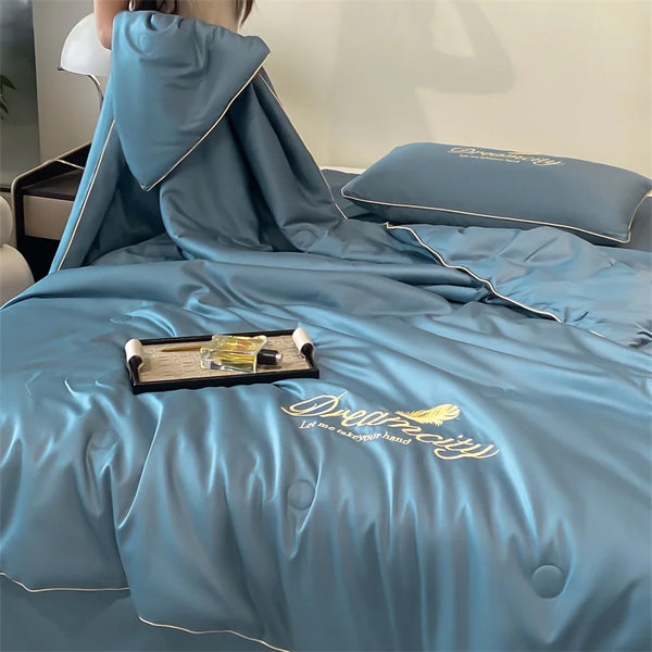 A teal ultra-soft ice silk fiber summer quilt draped over a bed, featuring embroidered text.