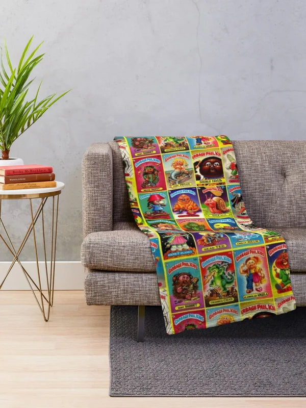 A colorful blanket featuring illustrations of wool sheep and related items draped over a gray sofa.