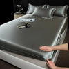 A smooth gray satin fitted sheet is draped over a mattress, with a small bottle and photos placed on the surface.