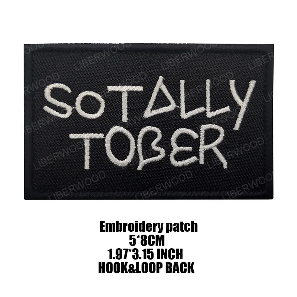 Black embroidered patch with the text SO TALLY TOBER in white thread.