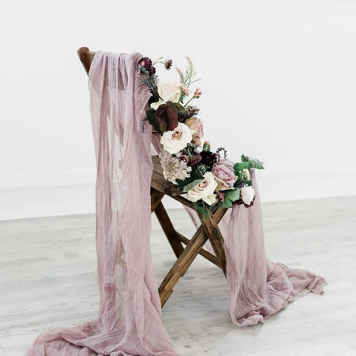 A dusty rose semi-sheer gauze table runner draped over a wooden easel decorated with dried flowers and greenery.