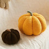 A bright orange fuzzy pumpkin shaped throw pillow resting on a white textured fabric.