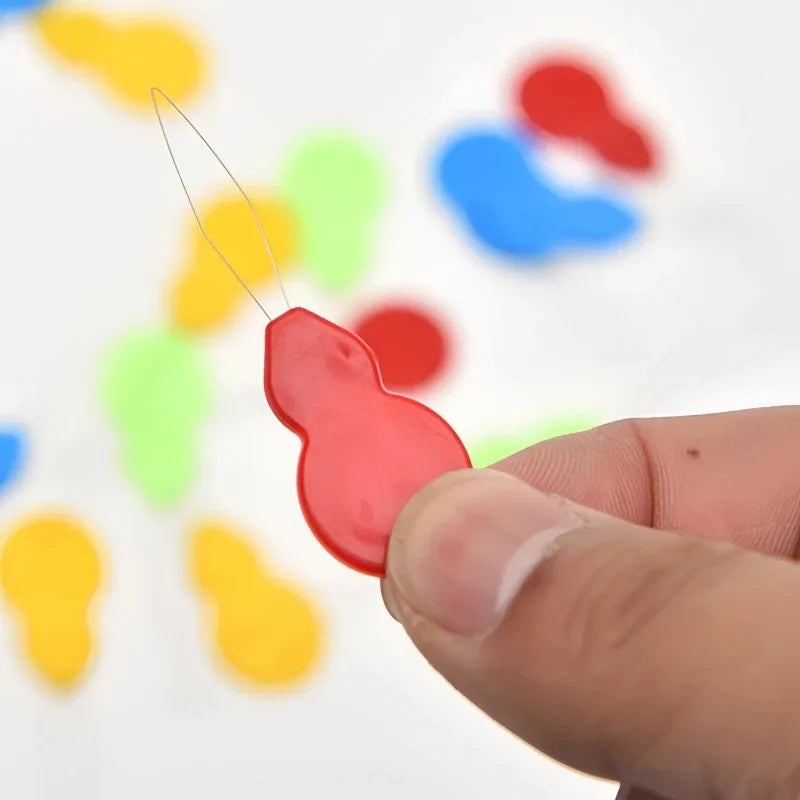 A hand is holding a red plastic threader from a set against a blurred background of colorful plastic shapes.