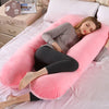 A woman relaxing on a pink U-shaped maternity body pillow on a bed.