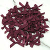 A pile of small, deep burgundy satin ribbon bows for crafts and decor.