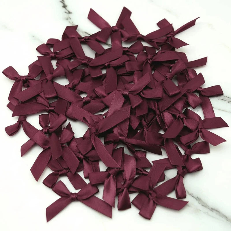 A pile of small, deep burgundy satin ribbon bows for crafts and decor.