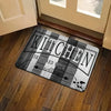 A rectangular kitchen mat with black and white stripes and text reads Kitchen Seasoned with Love placed on a wooden floor.