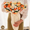 A hand knitted floral rose bouquet arrangement displayed with a white textured throw blanket and light yellow pants.