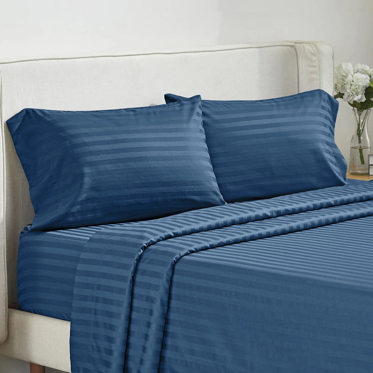 A navy blue striped bedding set featuring a duvet cover and pillows on a white upholstered bed.