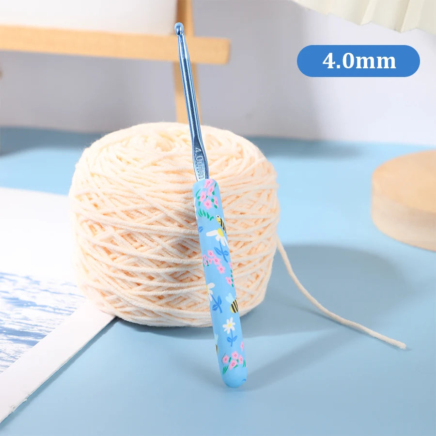 A blue ergonomic crochet hook with a floral design is shown next to a ball of light-colored yarn.