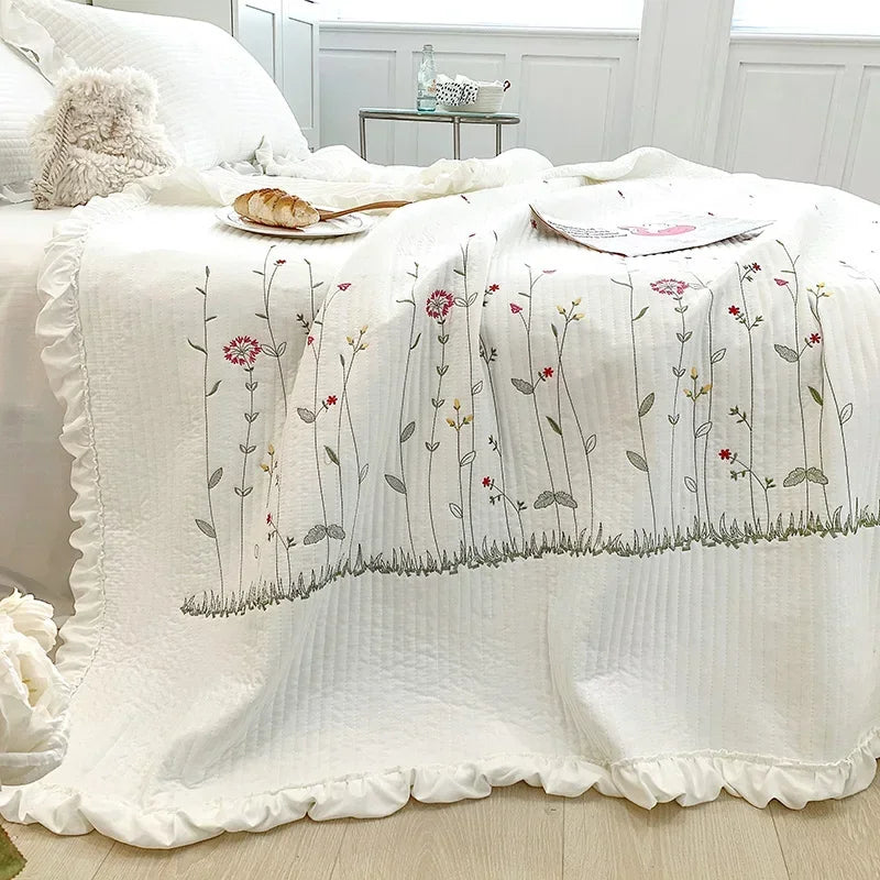 White quilt bedspread featuring delicate floral embroidery in muted pinks and greens.