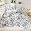 A light blue and white patterned quilt set featuring a main quilt, two pillows, and a blanket displayed on a white shelf.