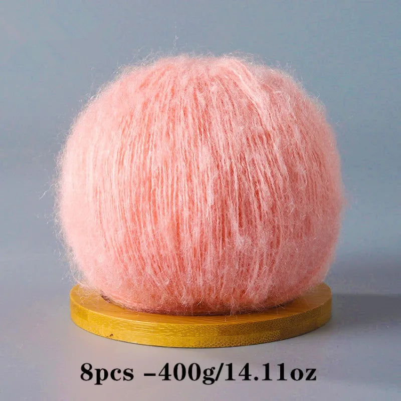 A ball of pink mohair yarn used for crafting, displayed on a wooden base.