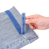 A hand is pulling a blue self-adhesive hem tape from the cuff of light blue denim fabric.