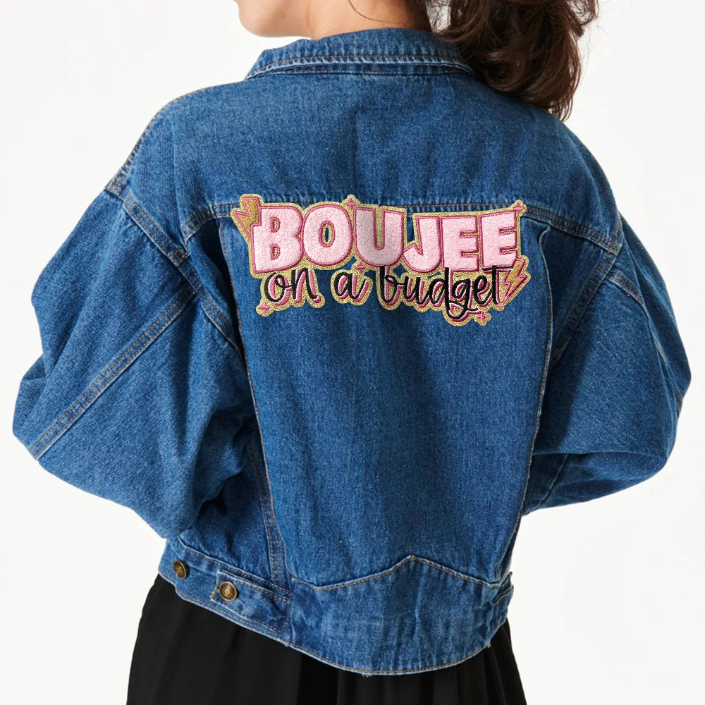 A denim jacket with pink embroidery on the back that reads BOUJEE on a budget