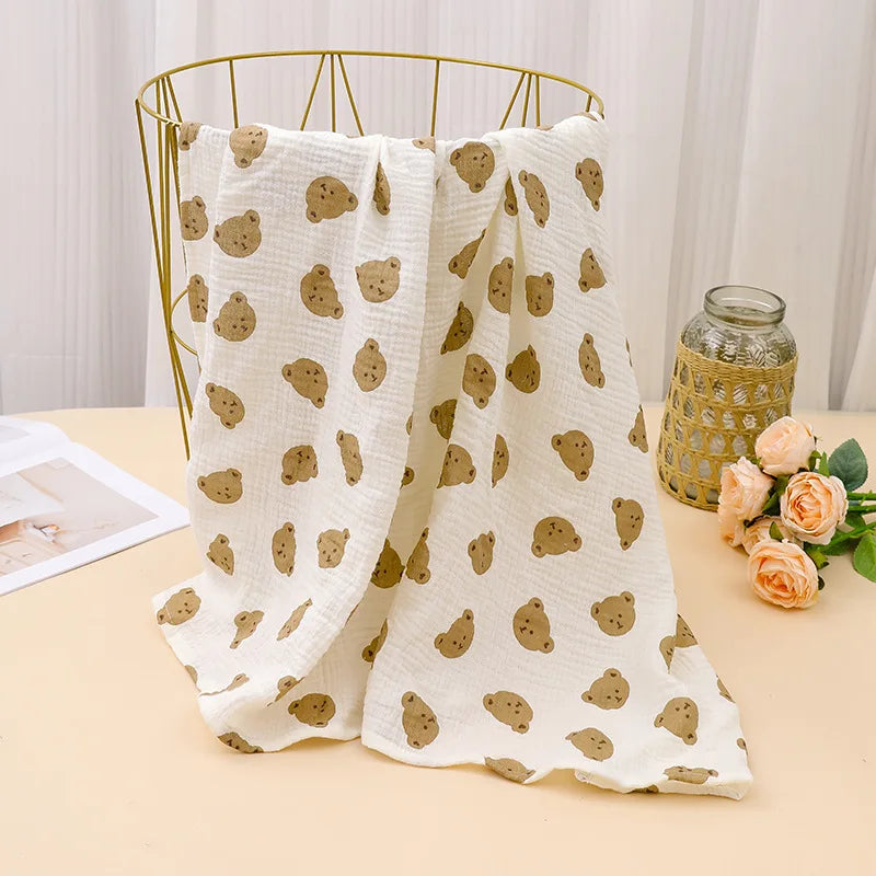 A beige printable cotton crib sheet with a pattern of small brown bears is draped over a gold wire hanger.