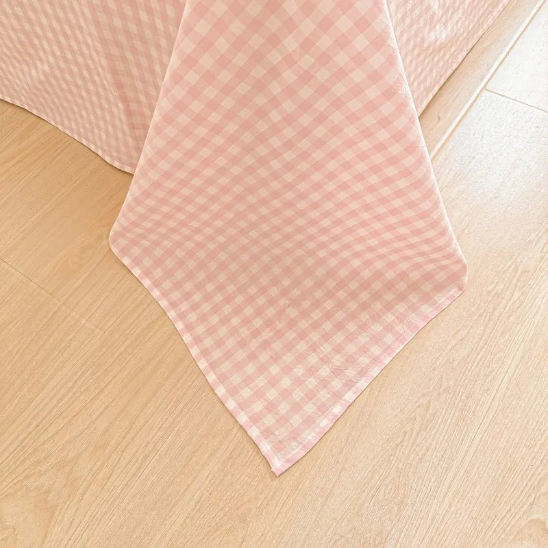 A pink gingham bed sheet or pillowcase laid flat on a light wooden floor.