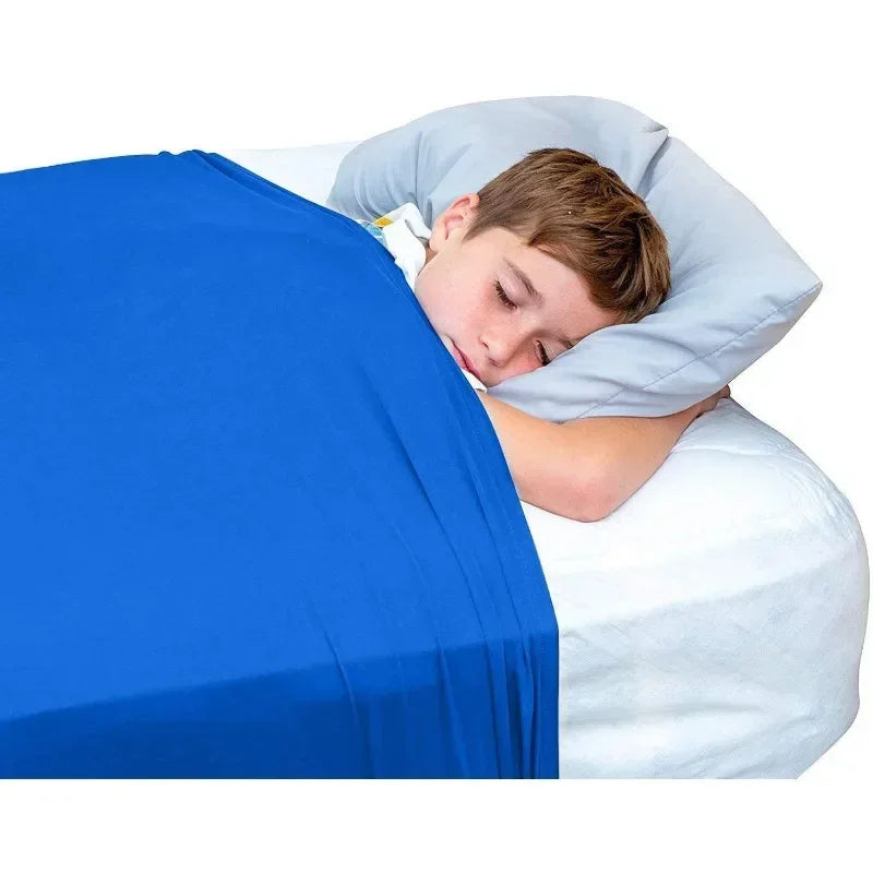 A young boy sleeping comfortably under a light blue pillow on a bright blue bed sheet.