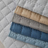 A stack of quilted anti-slip sofa covers in various shades of beige, gray, and blue.